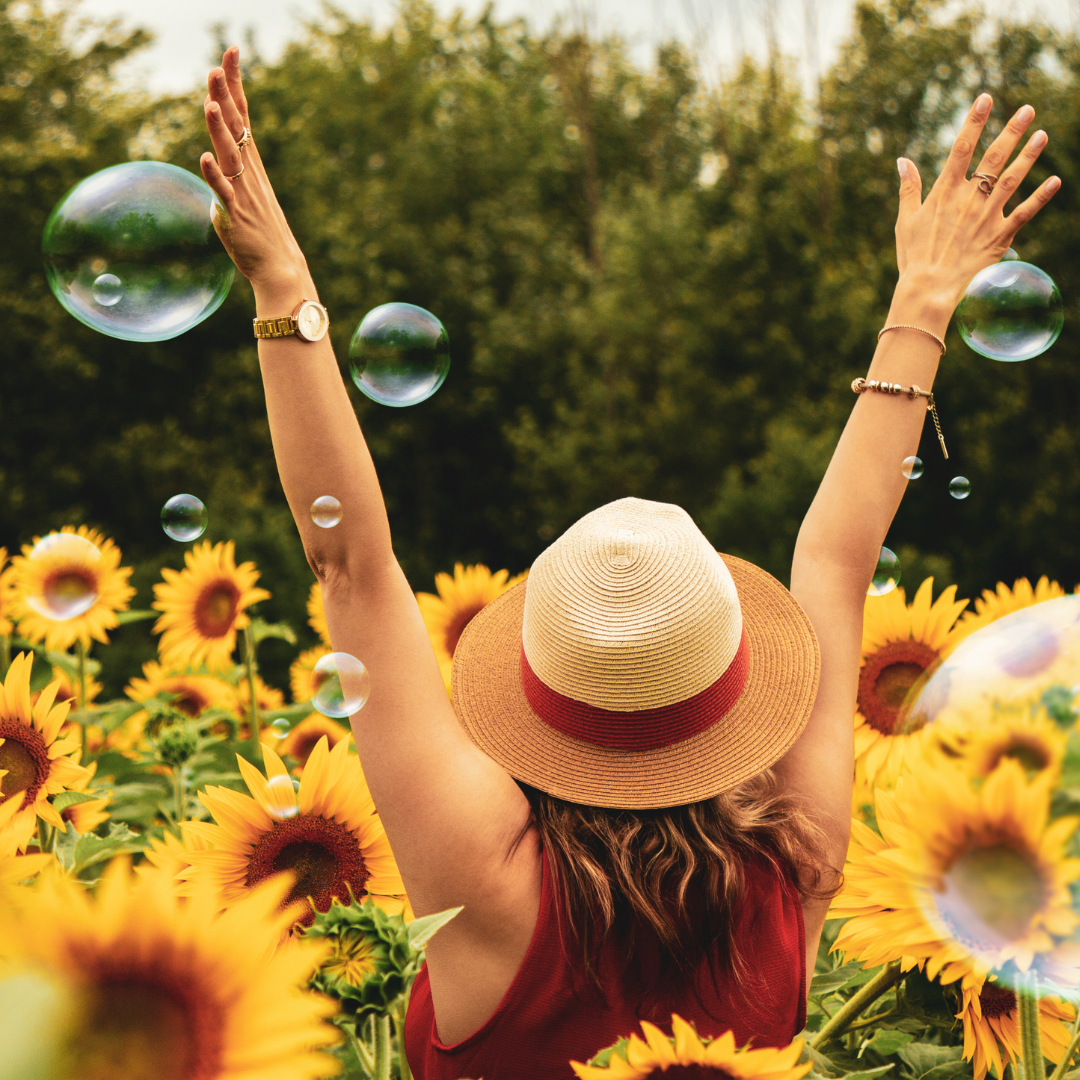 Person mit erhobenen Armen in einem Sonnenblumenfeld – Symbol für Lebensfreude, Energie und positives Wohlbefinden.